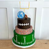 Three-tiered football-themed cake with decorative elements on a wooden surface.