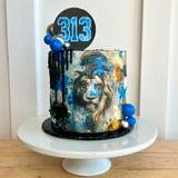 Cake with lion design and number 313 on a white stand against a white background